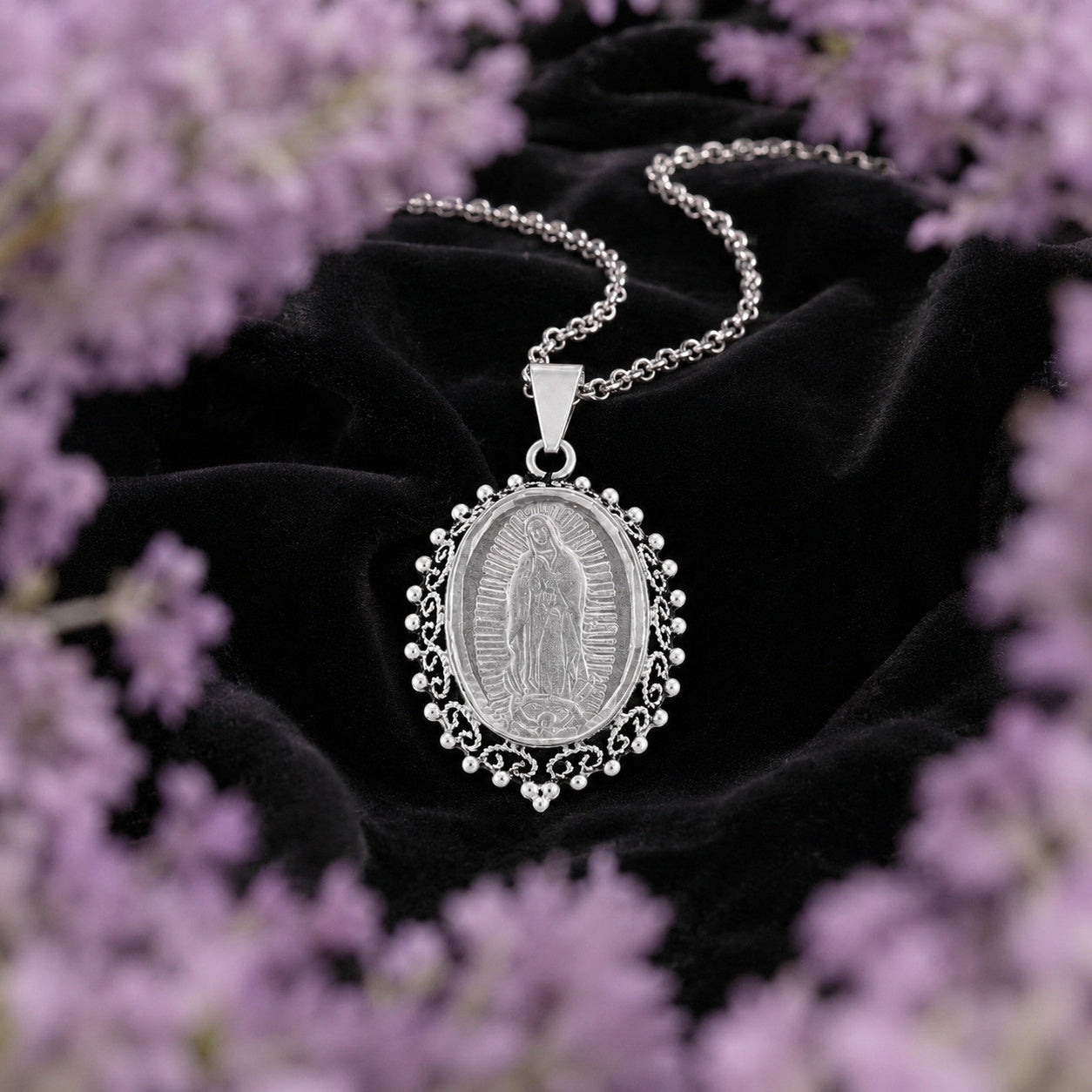 Dije de la Virgen de Guadalupe en plata ley .925 de Joyería Colibrí sobre terciopelo negro, enmarcado por un halo de lavanda