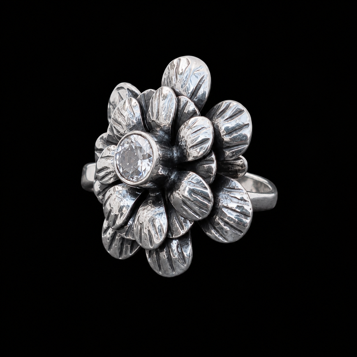 Anillo Flor con Circonia de plata ley .925 sobre fondo negro, con los pétalos grabados en capas y la circonia engarzada en bisel
