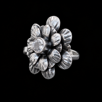 Anillo Flor con Circonia de plata ley .925 sobre fondo negro, con los pétalos grabados en capas y la circonia engarzada en bisel
